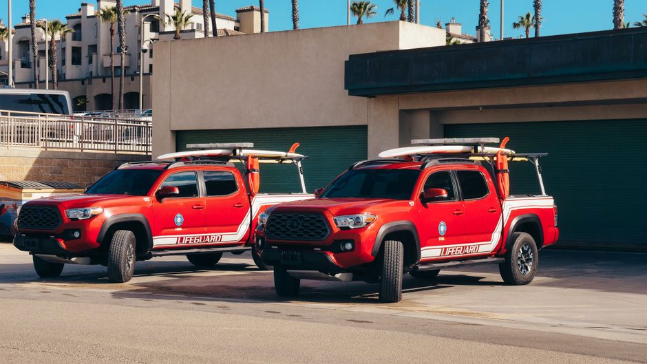 Two red lifeguard trucks parked on a sunny day near the beach.