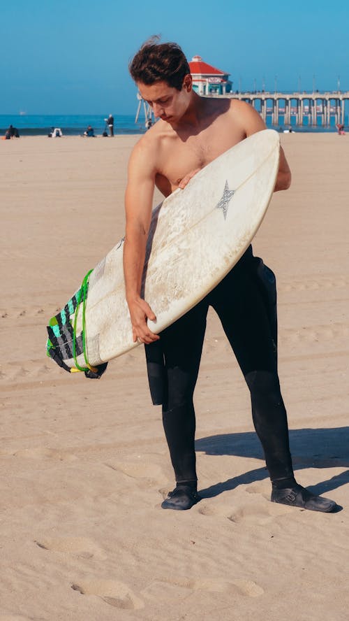 A Man in Black Pants Holding White Surfboard