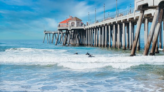 Surfers enjoy waves by the iconic Huntington Beach Pier on a sunny day.