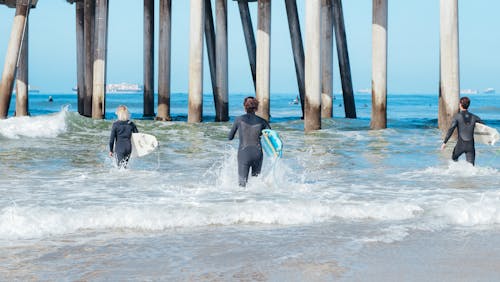 Man in Black Wet Suit Holding Blue Surfboard on Sea