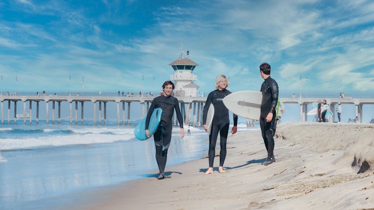 Surfers Walking On The Shore While Carrying Their Surfboards