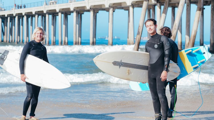 Surfers On The Shore Carrying Their Surfboards