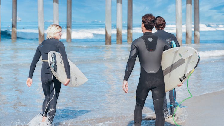 Surfers Walking On The Shore While Carrying Their Surfboards