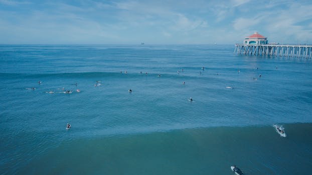Surfers catching waves near a famous pier on a clear sunny day.