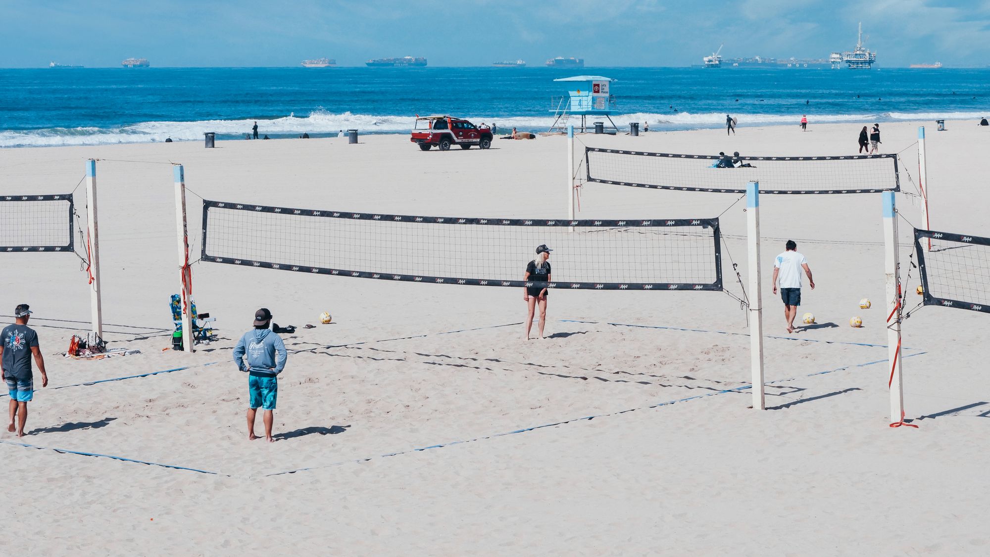 Flere beachvolleybaner ved havet med aktive spillere.