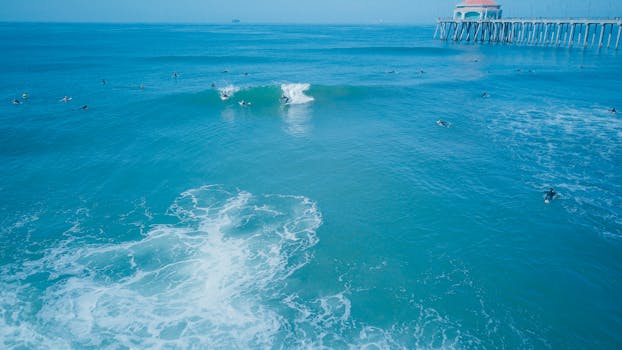 Aerial shot of surfers catching waves near Huntington Beach Pier in California.