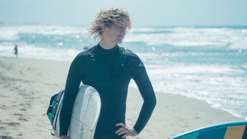 Free Caucasian male surfer with a surfboard on a sunny beach. Perfect for ocean lifestyle themes. Stock Photo