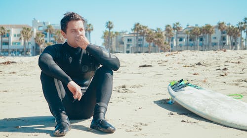 A Man in Black Wetsuit Sitting on the Sand