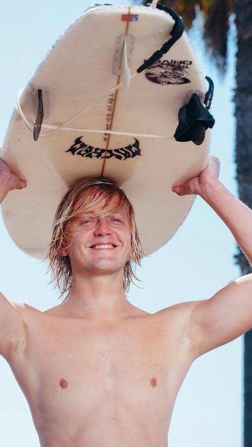 A Topless Man Carrying a Surfboard