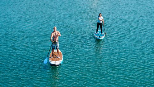 Free A man and woman enjoying standup paddleboarding on serene blue ocean water. Stock Photo