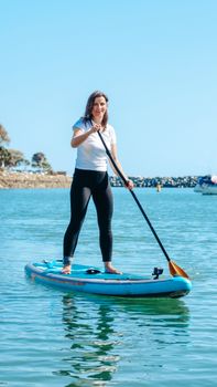 A woman enjoying standup paddleboarding on calm blue waters under a clear sky.