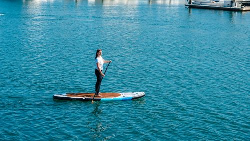 Free A woman enjoying paddle boarding on calm sea waters under a bright summer sun. Stock Photo
