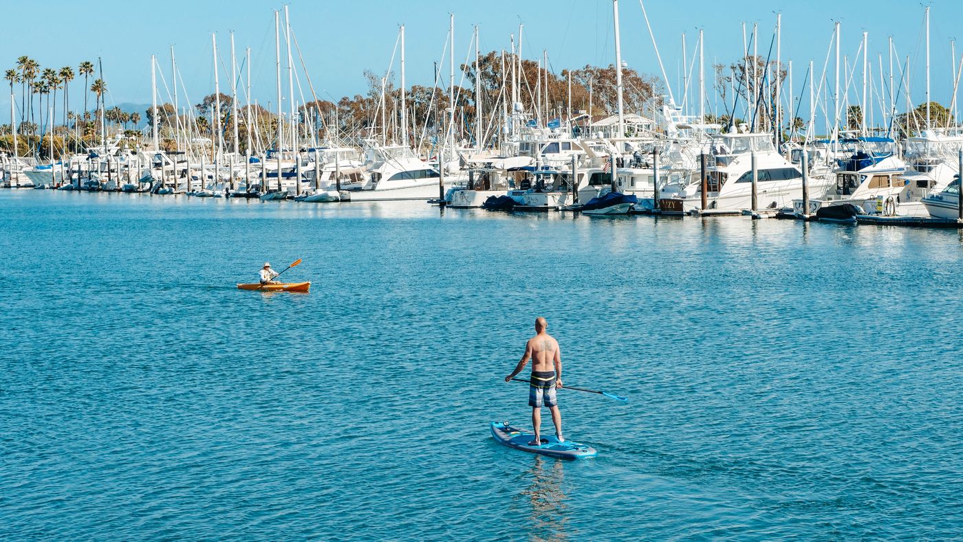 Kayaker and paddleboarder moving across calm coastal water