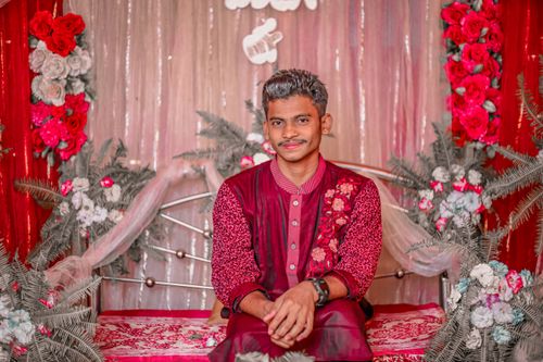 Free A man in vibrant traditional attire poses amid floral decorations indoors, showcasing Bangladeshi cultural elegance. Stock Photo
