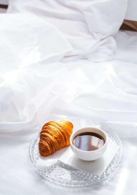 Enjoy a warm croissant and coffee on a comfortable bed with white linens.