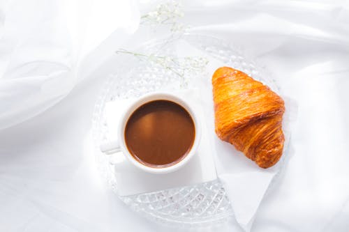 Free Close-Up Photo of a Cup of Coffee and a Croissant on a Glass Plate Stock Photo