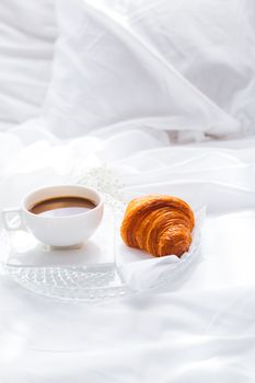 A serene setup of coffee and croissant on a bed, showcasing a cozy French breakfast scene.