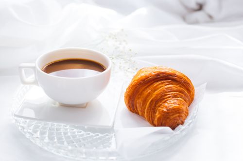 Free A serene breakfast scene featuring a cup of coffee and a fresh croissant on elegant white linens. Stock Photo