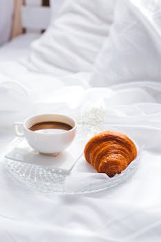 A cozy breakfast setup with a croissant and coffee on a bed. Perfect to start your day with elegance.