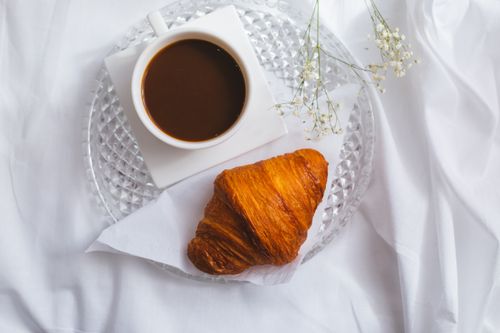 Free Top view of a French breakfast featuring a croissant and coffee on a glass plate, set on white linen. Stock Photo