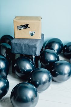 Elegant birthday celebration with a gift on a chair surrounded by black balloons in a minimalist indoor setting.