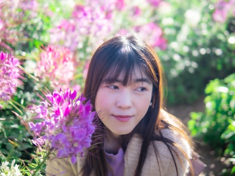 A young woman surrounded by vibrant pink flowers on a sunny day, creating a serene and joyful atmosphere.