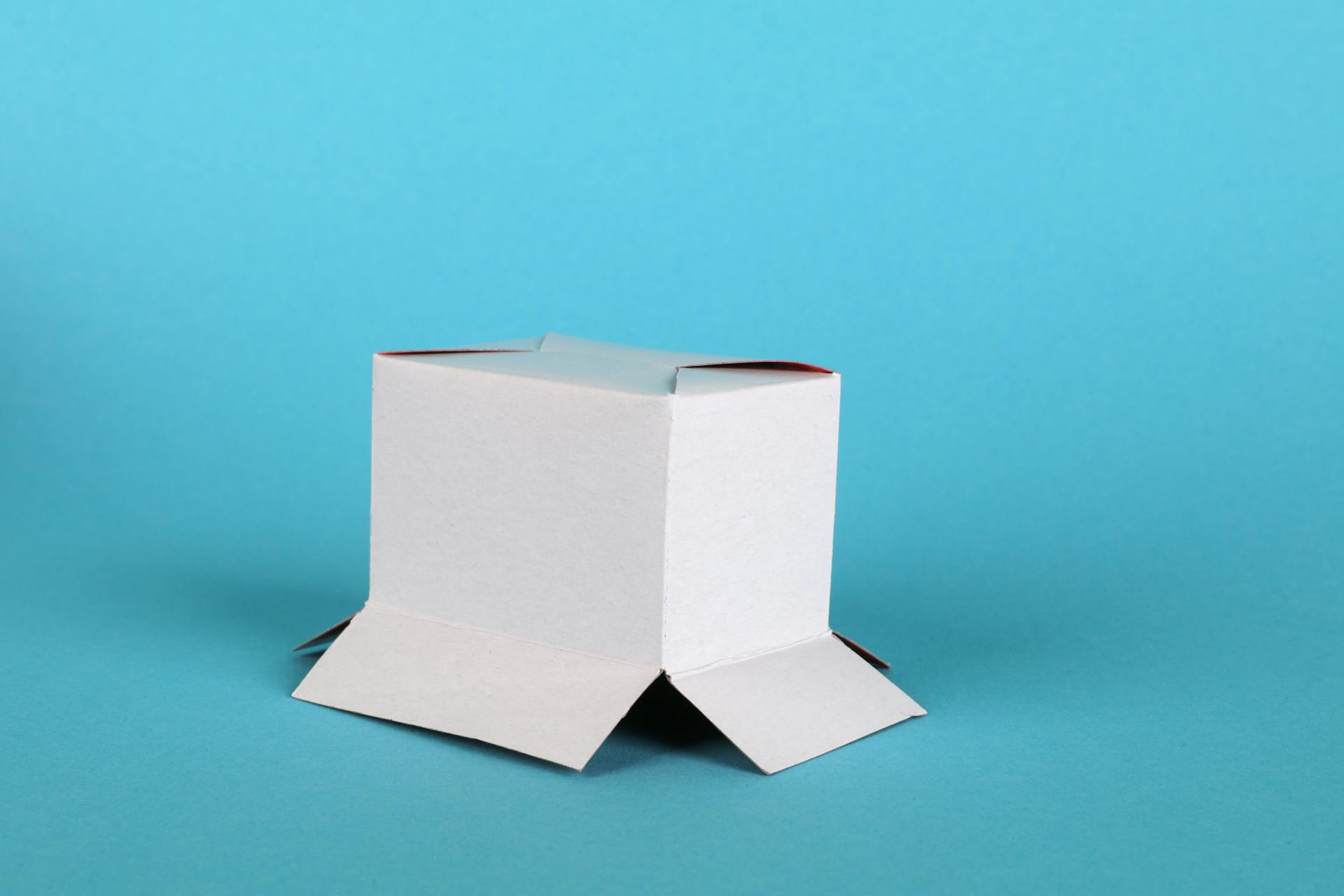 White cardboard box with open flaps on a blue backdrop, perfect for packaging or presentation themes.