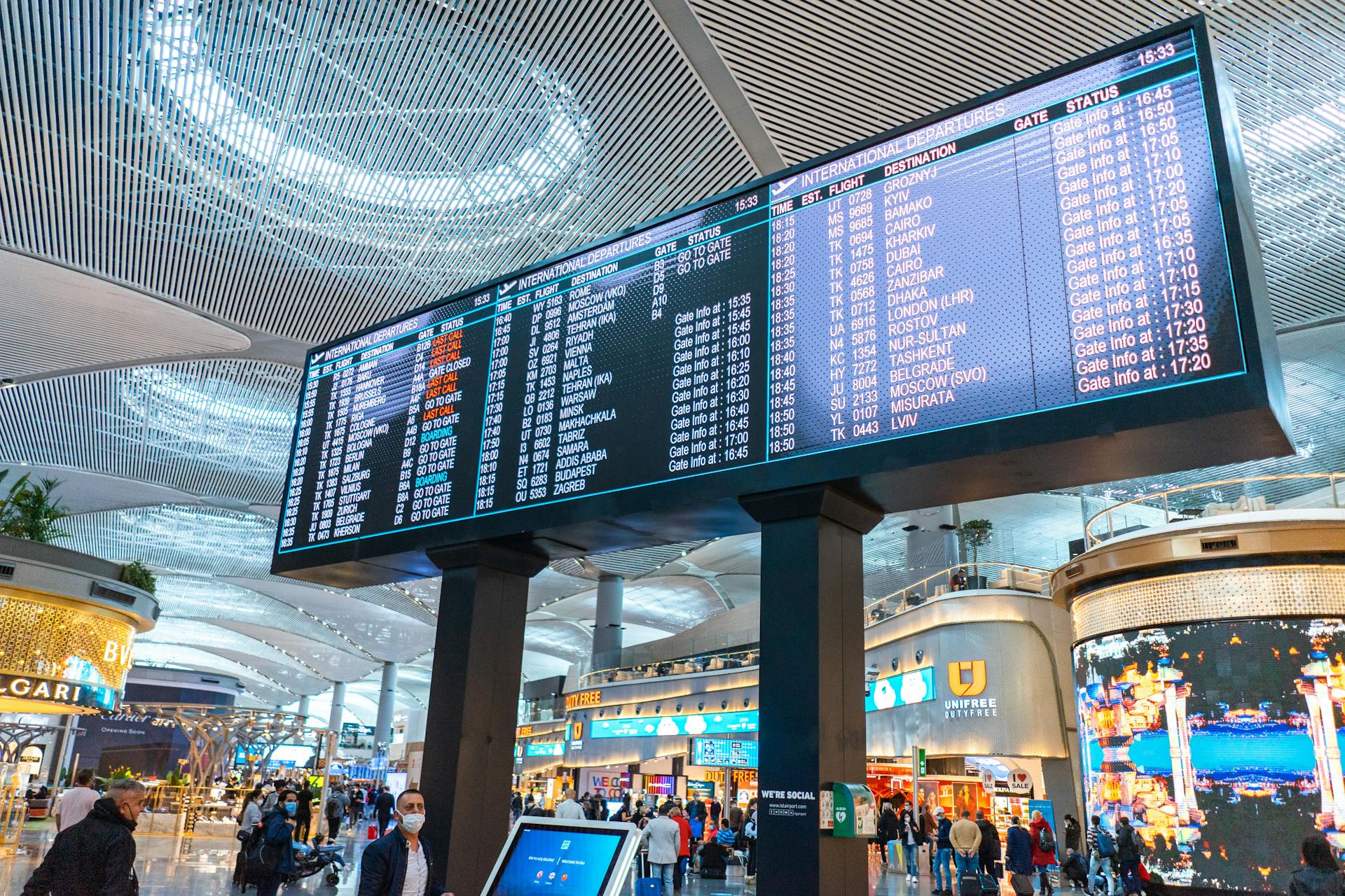 Passengers walk through Istanbul Airport's departure area, surrounded by stores and flight information displays.