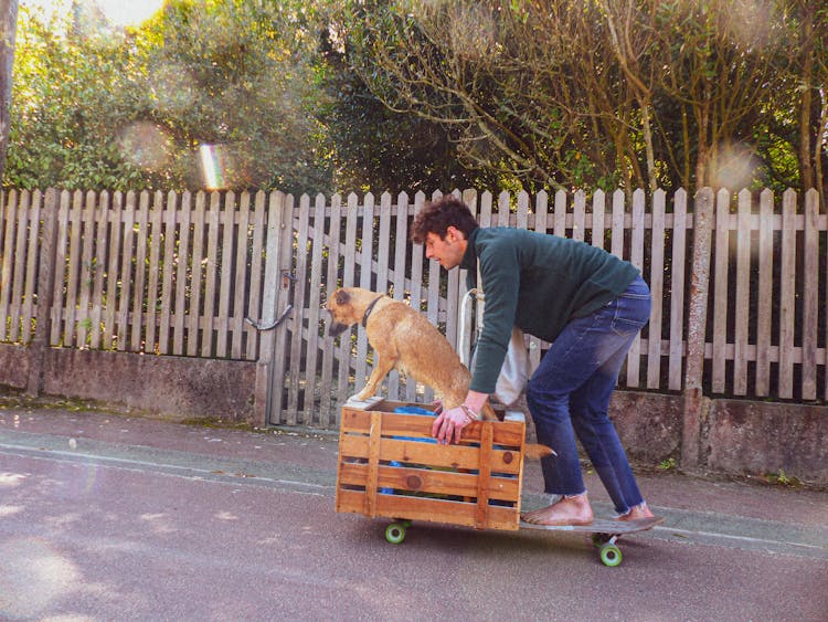 A Man Riding A Skateboard With His Dog On A Wooden Crate 