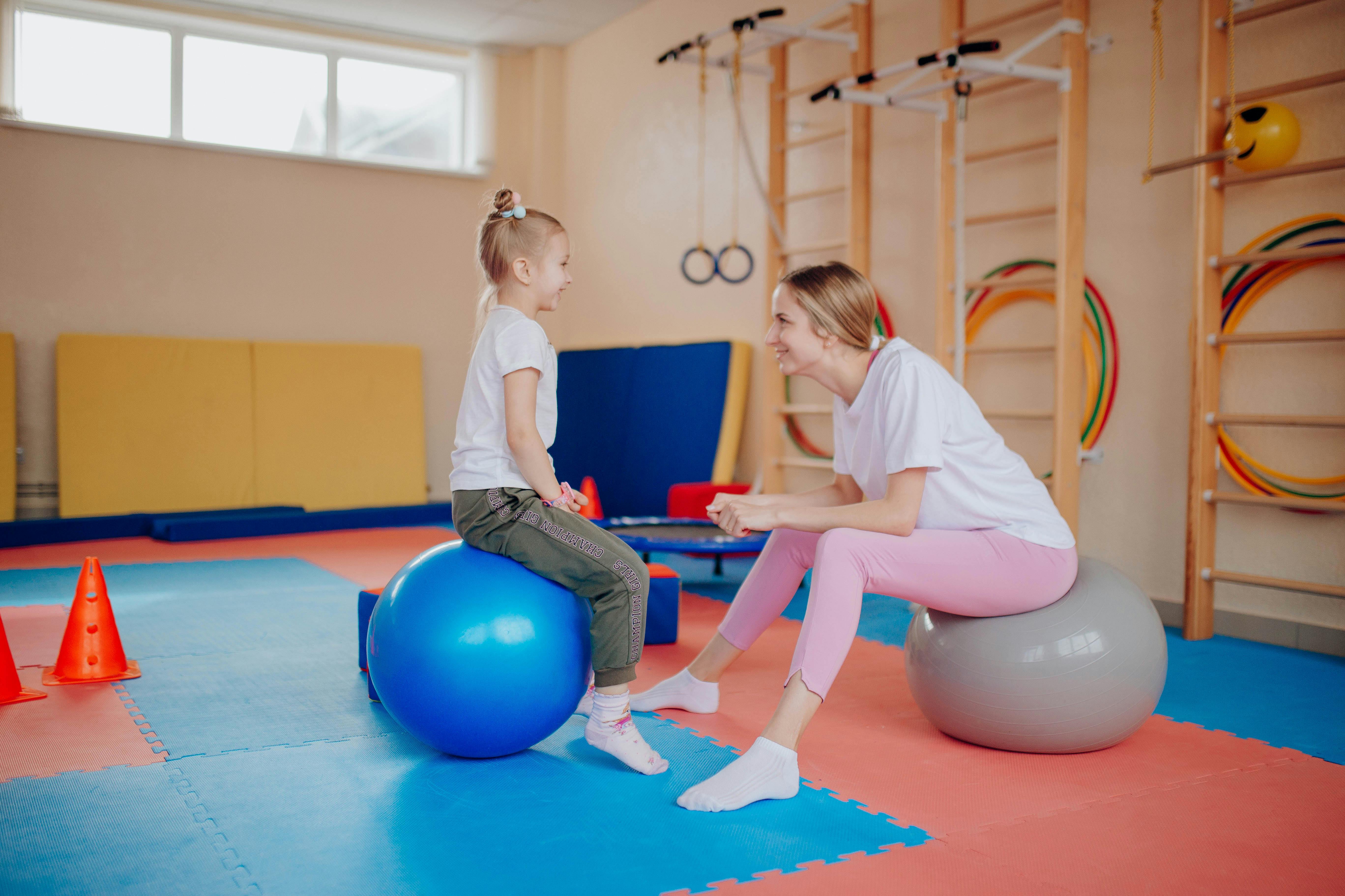 Happy mother and daughter bonding on exercise balls in an indoor gym setting.