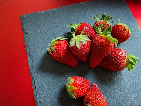 Vibrant red strawberries arranged on a dark slate plate, capturing freshness and color contrast.