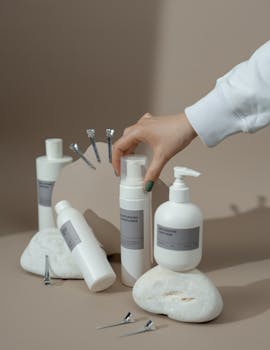 Elegant display of skincare bottles with a hand reaching for one, set against a beige backdrop.