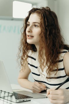 A focused businesswoman taking notes and working on her laptop in an office.