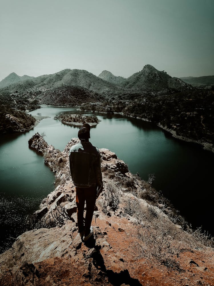 Person Standing On Top Of Mountain Near Body Of Water 