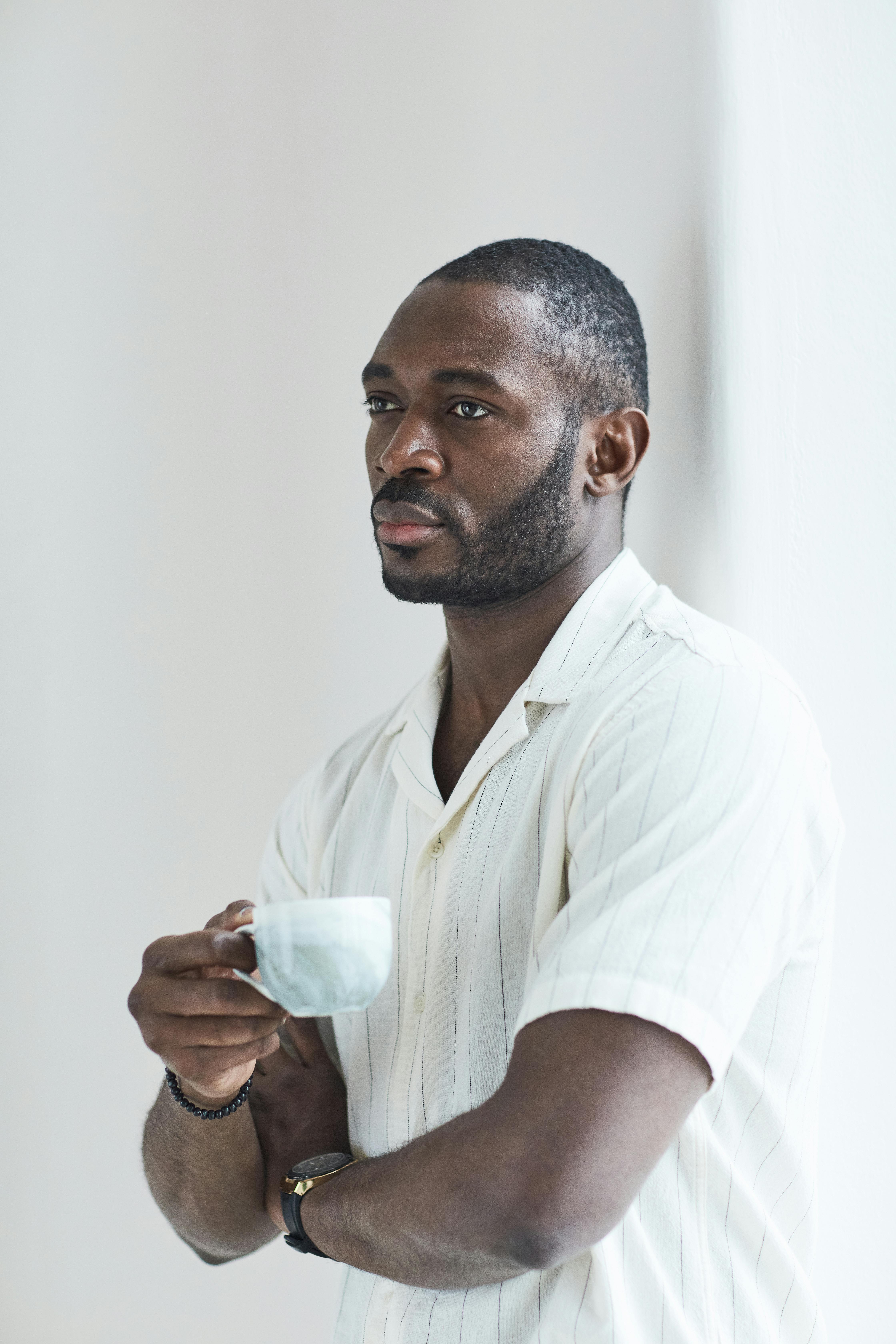 African American man in a white polo shirt enjoying a coffee break indoors.