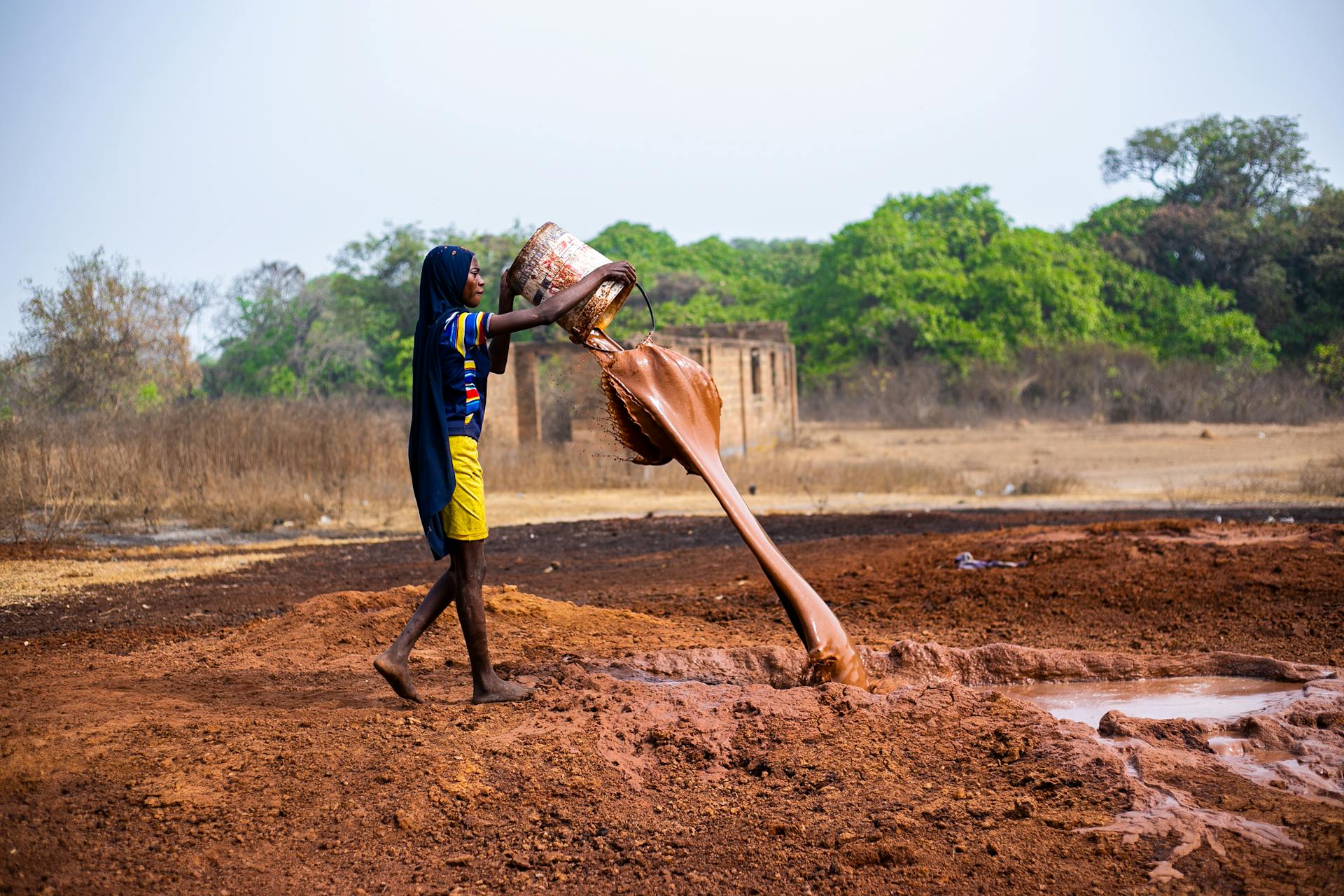 Person Pouring Mud From a Bucket on a Field