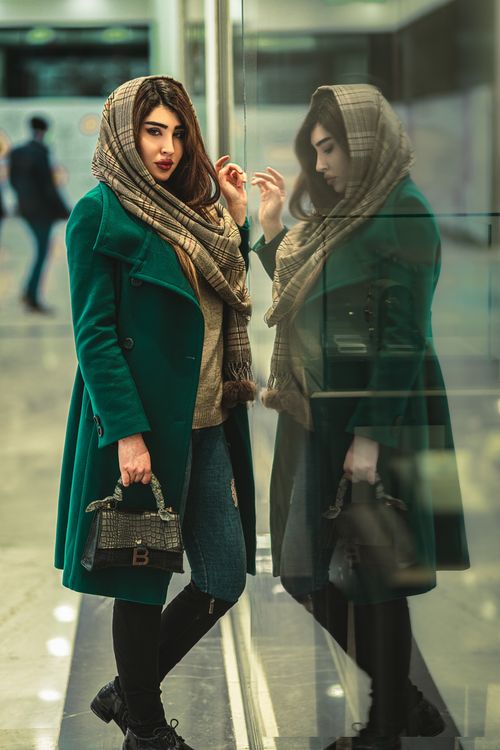 Free Fashionable woman in green coat leaning against glass with stylish reflection. Stock Photo