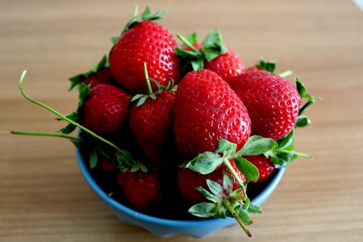 Close-up of fresh, ripe strawberries in a blue bowl on a wooden surface, highlighting their vibrant color and texture.