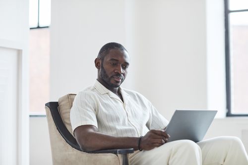 Free African American man with a beard works on a laptop indoors, wearing a button-down shirt. Stock Photo