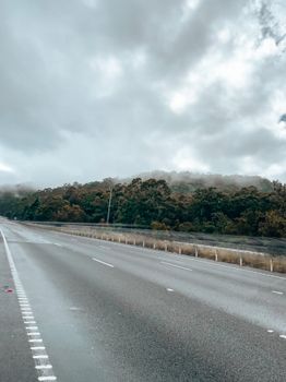 Empty concrete road through a misty forest under a cloudy sky.