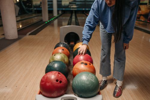 Free A woman in casual attire selecting a colorful bowling ball at a bowling alley. Stock Photo