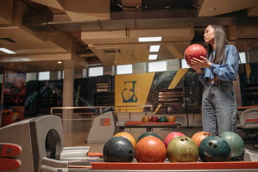 A woman is selecting a bowling ball in a vibrant, contemporary bowling alley.