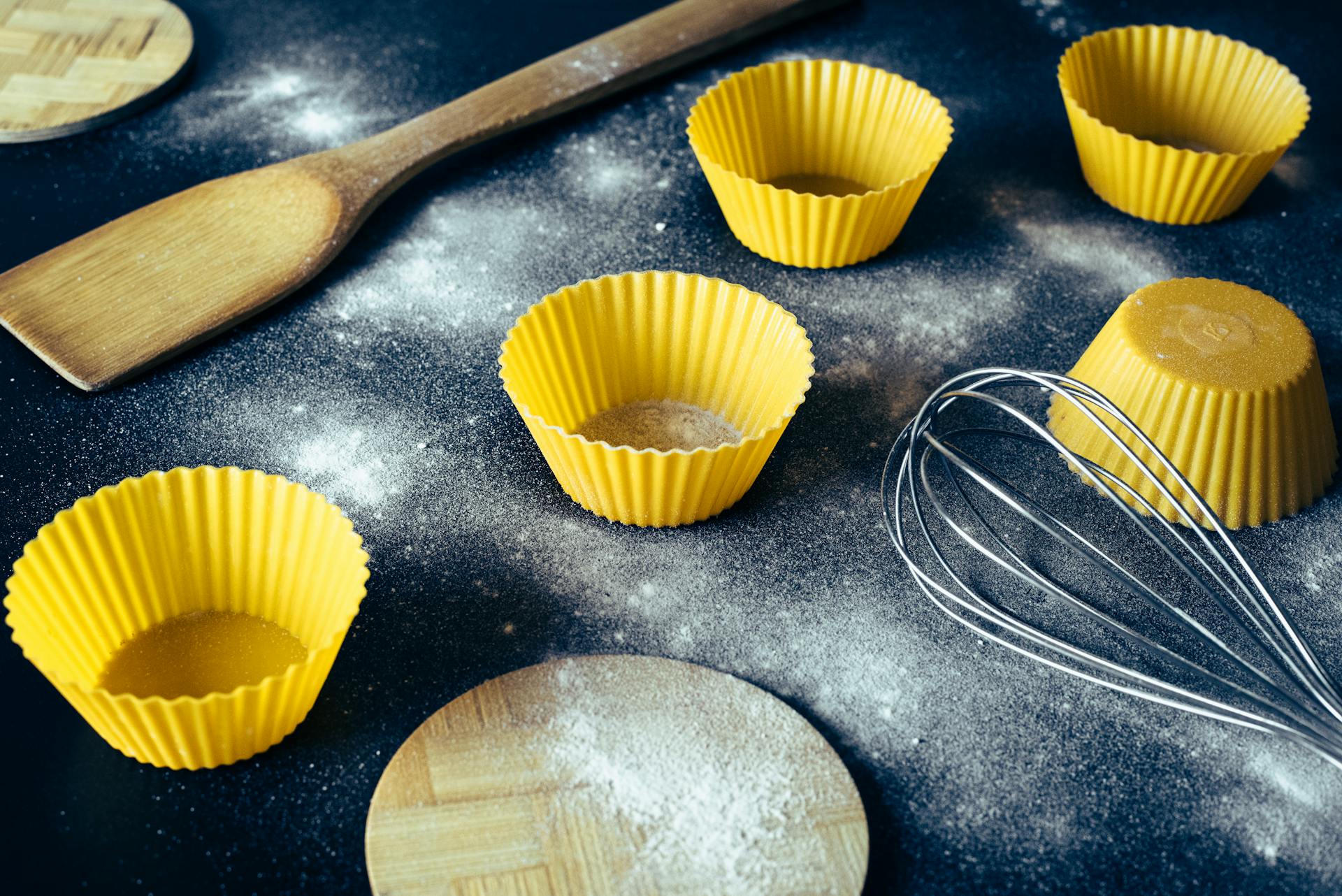 From above of yellow cupcake molds and cooking utensils placed on dirty table with flour