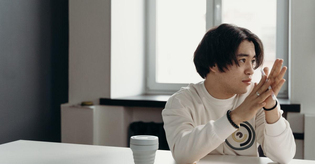 person holding a coffee cup with a notebook and pen, looking thoughtfully out a window