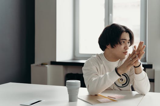 A young man in an office setting deep in thought with a coffee cup nearby, creating a focused work atmosphere.