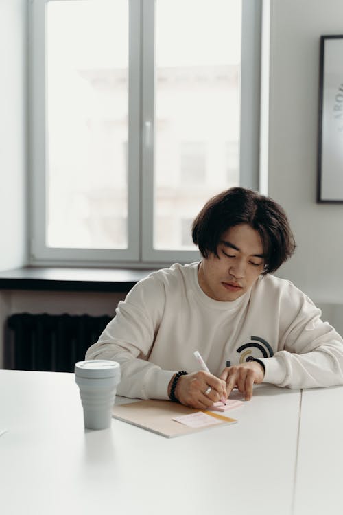 Man in White Sweater Writing on a Notepad