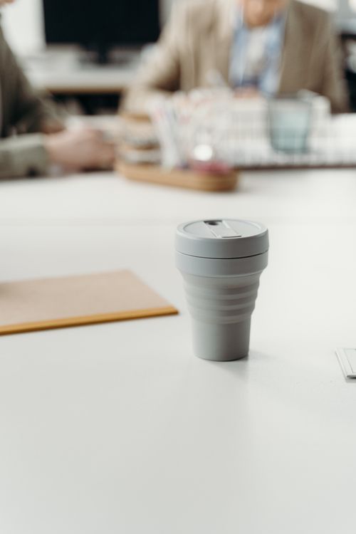 Free A reusable coffee cup on a desk in an office, promoting sustainability and eco-friendliness. Stock Photo