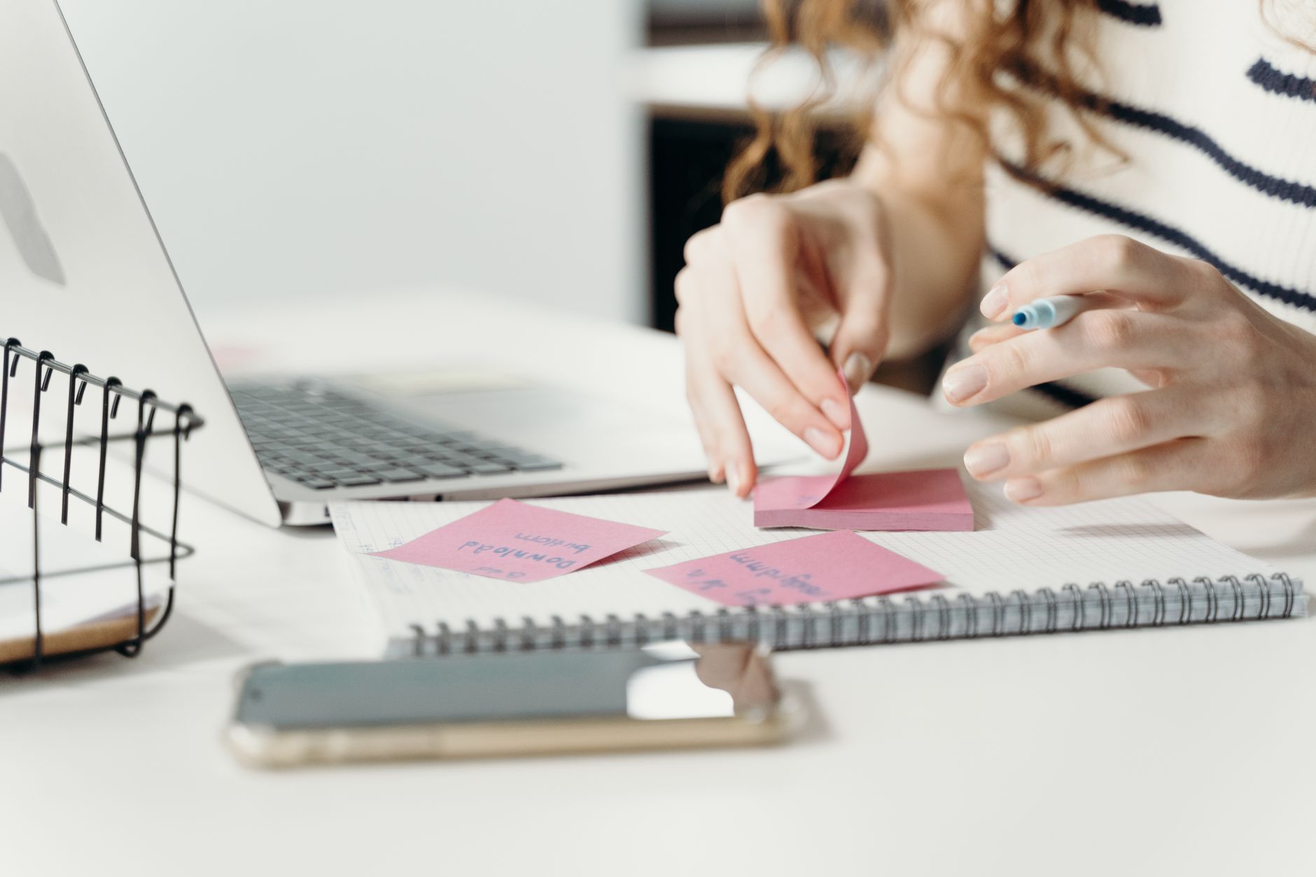 How to Organize Content Ideas Using Only Your Phone Woman organizing notes with a laptop and smartphone at a modern workplace.