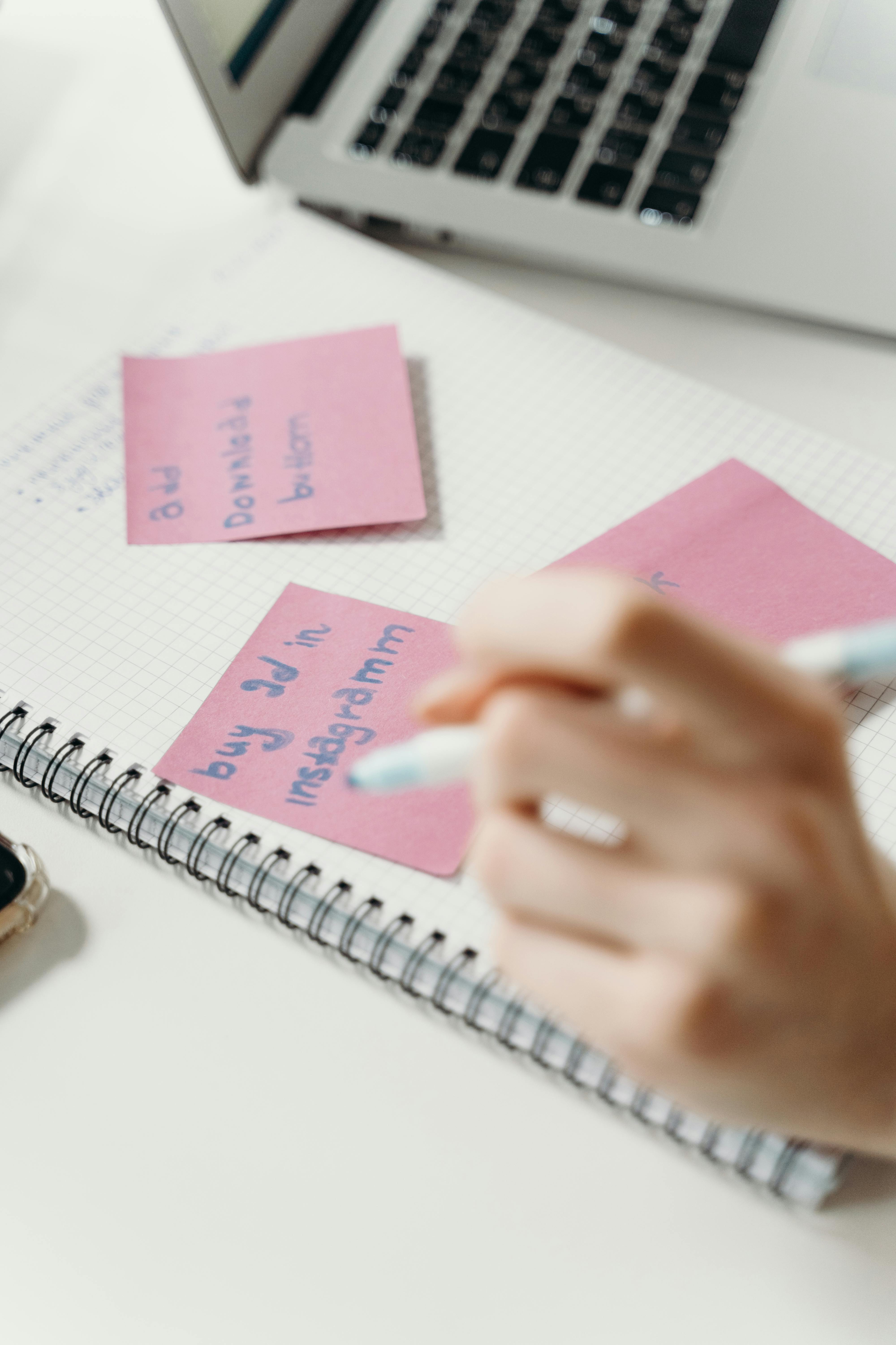 person writing on pink sticky notes