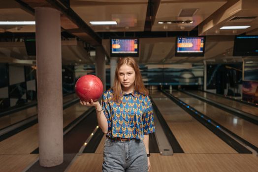 Woman in casual attire holding a bowling ball at a brightly lit alley.